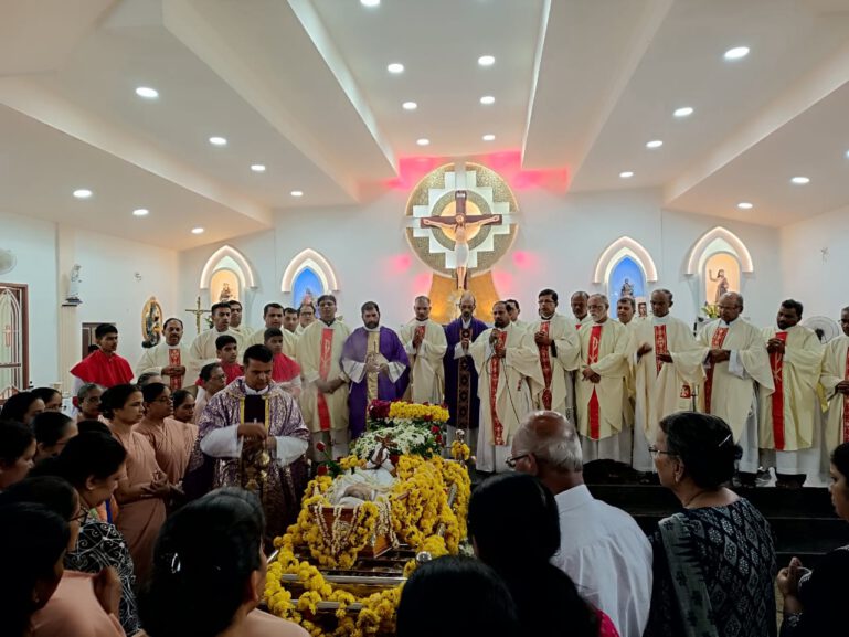 der blumengeschmückte Sarg und Geistliche bei der Trauerfeier für Sr. Kalyani.
